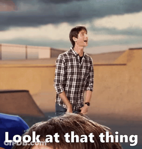 A Man In A Plaid Shirt Is Standing In Front Of A Sign That Says " Look At That Thing " GIF