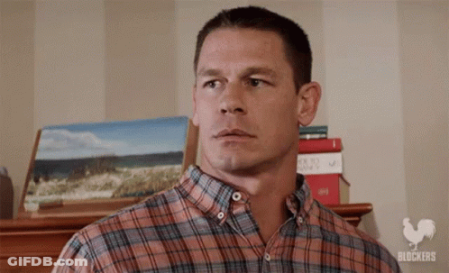 A Man In A Plaid Shirt Is Standing In Front Of A Stack Of Books And A Painting . GIF