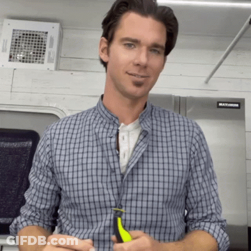 A Man In A Plaid Shirt Is Standing In Front Of A Stainless Steel Refrigerator That Says Maximum GIF