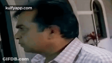 A Man In A Plaid Shirt Is Standing In Front Of A Window And Looking At Something . GIF