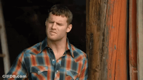 A Man In A Plaid Shirt Is Standing In Front Of A Wooden Building . GIF
