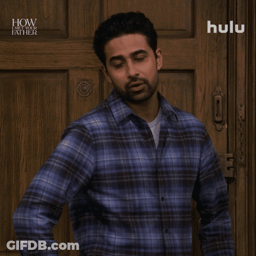 A Man In A Plaid Shirt Is Standing In Front Of A Wooden Door And Says No Big Deal GIF