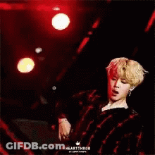 A Man In A Plaid Shirt Is Standing On A Stage With A Red Background . GIF
