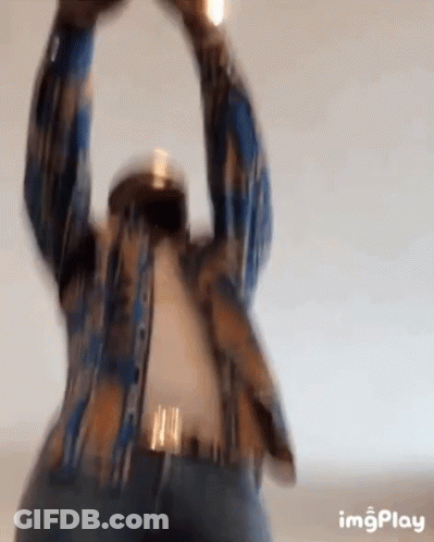 A Man In A Plaid Shirt Is Standing With His Arms In The Air . GIF