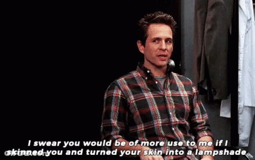 A Man In A Plaid Shirt Is Talking On A Phone While Sitting In A Chair . GIF