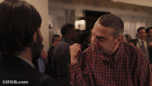 A Man In A Plaid Shirt Is Talking To Another Man In A Crowd GIF