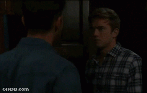 A Man In A Plaid Shirt Is Talking To Another Man GIF