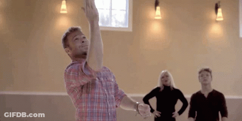 A Man In A Plaid Shirt Is Throwing A Frisbee In The Air While A Group Of People Are Watching . GIF