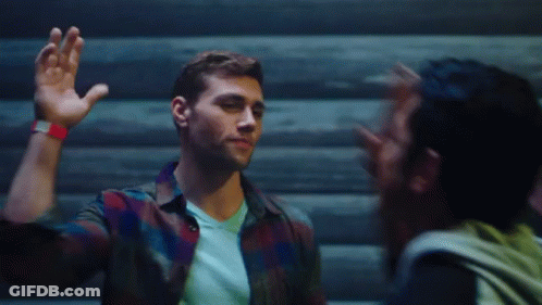 A Man In A Plaid Shirt Is Waving His Hand At Another Man GIF