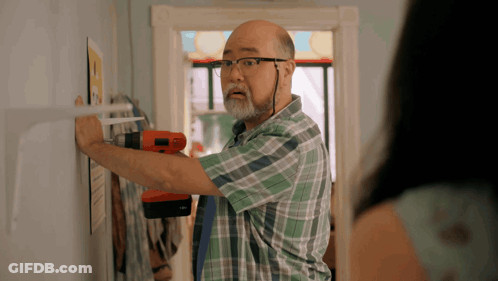 A Man In A Plaid Shirt Is Working On A Wall GIF