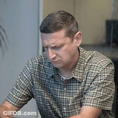 A Man In A Plaid Shirt Looks Down With A Serious Look On His Face GIF