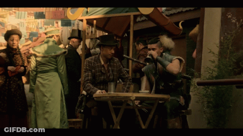 A Man In A Plaid Shirt Sits At A Table Drinking From A Glass GIF
