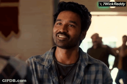 A Man In A Plaid Shirt Smiles In Front Of A Sign That Says X7wickreddy GIF