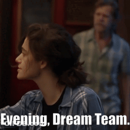 A Man In A Plaid Shirt Stands In A Crowd With The Words Evening Dream Team Written Below Him GIF