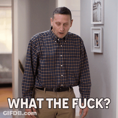 A Man In A Plaid Shirt Stands In A Hallway And Says " What The Fuck " GIF