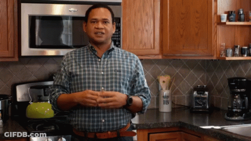 A Man In A Plaid Shirt Stands In A Kitchen In Front Of A Microwave And A Container With The Letter B On It GIF