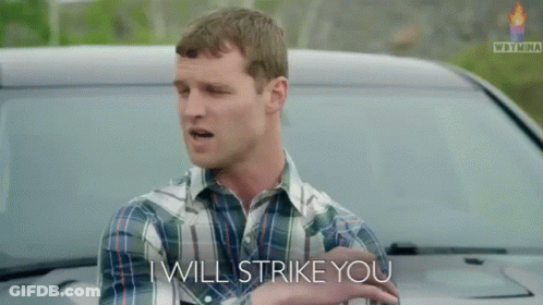 A Man In A Plaid Shirt Stands In Front Of A Car And Says I Will Strike You GIF