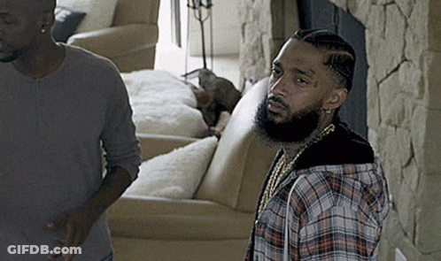 A Man In A Plaid Shirt Stands Next To Another Man In A Living Room GIF