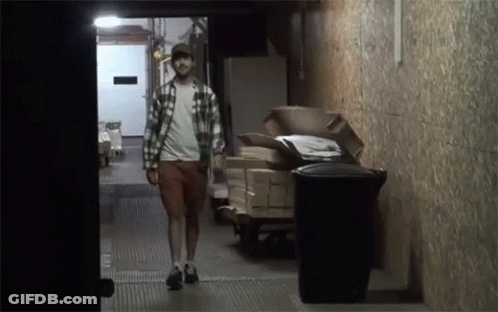 A Man In A Plaid Shirt Walks Down A Hallway GIF