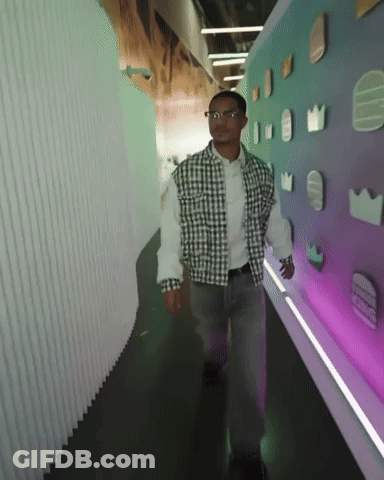 Man In Plaid Shirt Walking Down Hallway With Purple Wall GIF