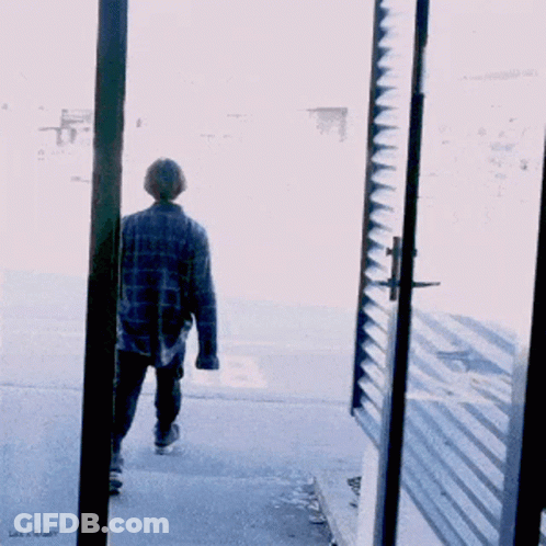 A Man In A Plaid Shirt Walks Down The Street GIF