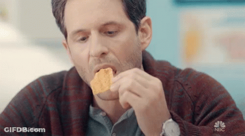 A Man In A Plaid Sweater Is Eating A Piece Of Tortilla Chips . GIF