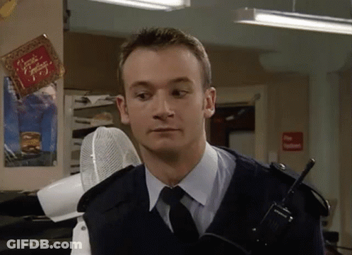 A Man In A Police Uniform And Tie Is Holding A Walkie Talkie In A Room . GIF