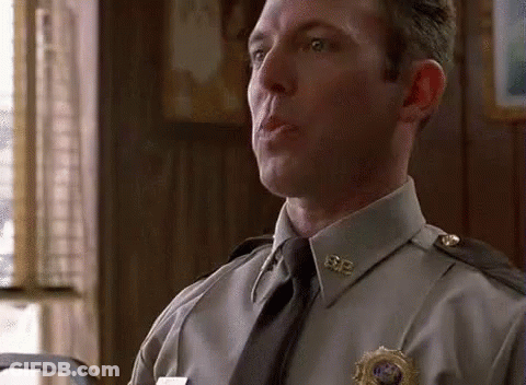 A Man In A Police Uniform And Tie Is Sitting In A Room Talking To Someone . GIF