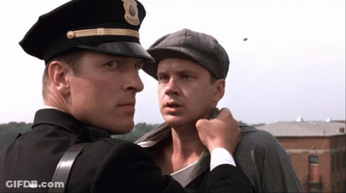 A Man In A Police Uniform Holds Another Man 'S Neck GIF