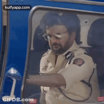 A Man In A Police Uniform Is Driving A Blue Vehicle . GIF