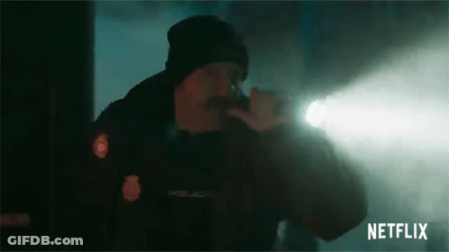A Man In A Police Uniform Is Holding A Flashlight In His Hand . GIF