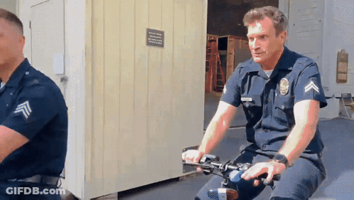 A Man In A Police Uniform Is Riding A Bike In Front Of A Building GIF