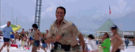A Man In A Police Uniform Is Running On A Beach With People . GIF