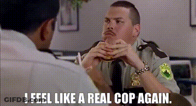 A Man In A Police Uniform Is Sitting At A Table With Another Man And Eating A Hamburger . GIF
