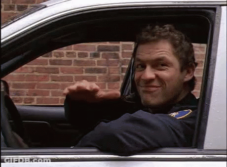 A Man In A Police Uniform Is Sitting In A Car And Waving . GIF