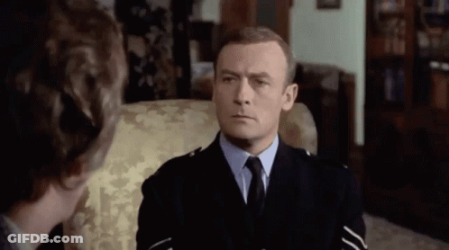 A Man In A Police Uniform Is Sitting In A Chair And Talking To Another Man . GIF