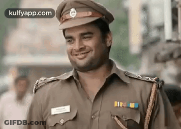 A Man In A Police Uniform Is Smiling While Standing On A Street . GIF
