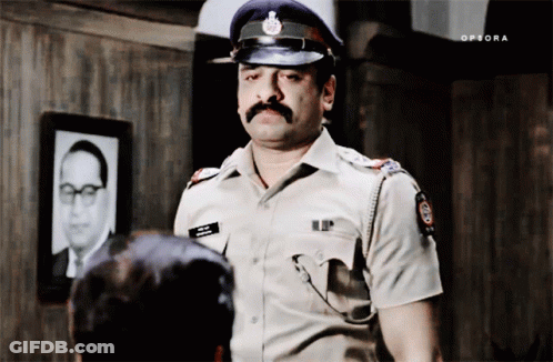 A Man In A Police Uniform Is Standing In Front Of A Picture Of A Man With A Mustache GIF