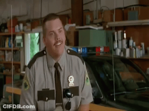 A Man In A Police Uniform Is Standing In Front Of A Police Car . GIF