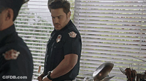 A Man In A Police Uniform Is Standing In Front Of A Window GIF