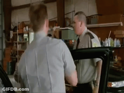 A Man In A Police Uniform Is Talking To Another Man In A Garage While Standing Next To A Car . GIF