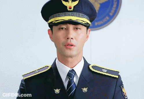 A Man In A Police Uniform Stands In Front Of A Police Logo GIF
