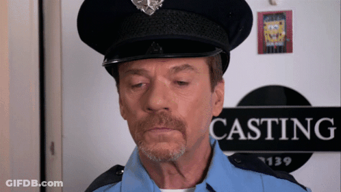 A Man In A Police Uniform Stands In Front Of A Sign That Says Casting GIF