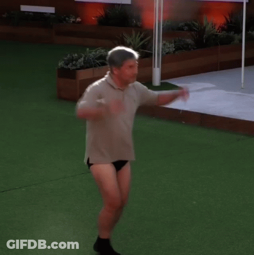 A Man In A Polo Shirt And Black Underwear Is Standing On A Lush Green Field GIF