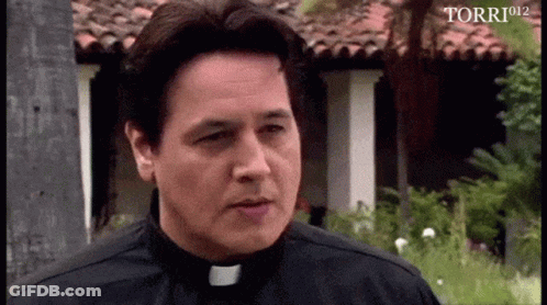 A Man In A Priest 'S Collar Is Standing In Front Of A Building With Torri912 Written In The Corner GIF