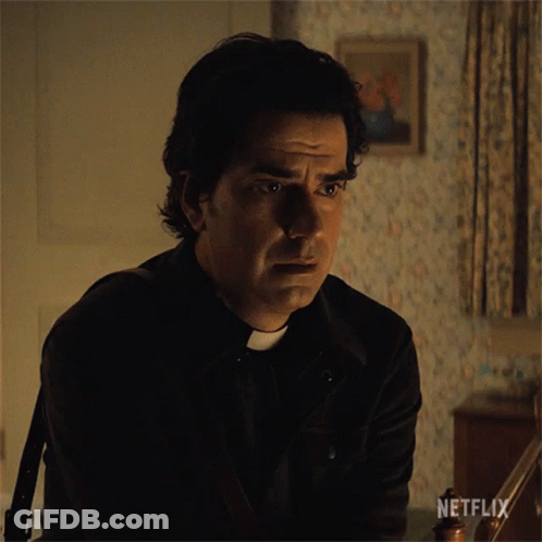 A Man In A Priest 'S Outfit Is Sitting In A Dark Room With A Netflix Logo On The Bottom Right GIF