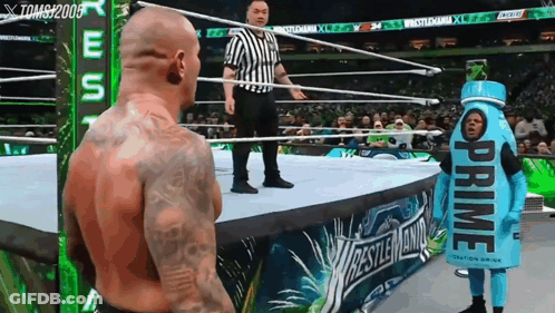 A Man In A Prime Costume Stands In A Wrestling Ring With A Referee GIF
