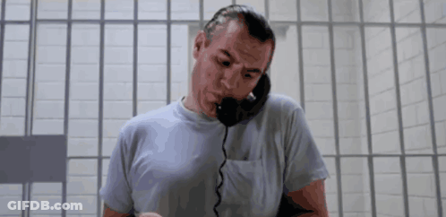 A Man In A Prison Cell Talking On A Phone GIF