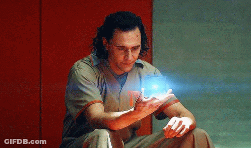 A Man In A Prison Uniform Is Sitting On The Floor Holding A Blue Object In His Hand . GIF