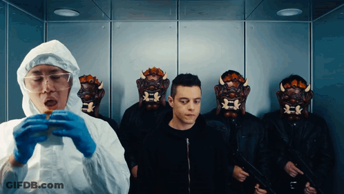 A Man In A Protective Suit Is Eating A Hamburger In Front Of A Group Of Men Wearing Masks GIF